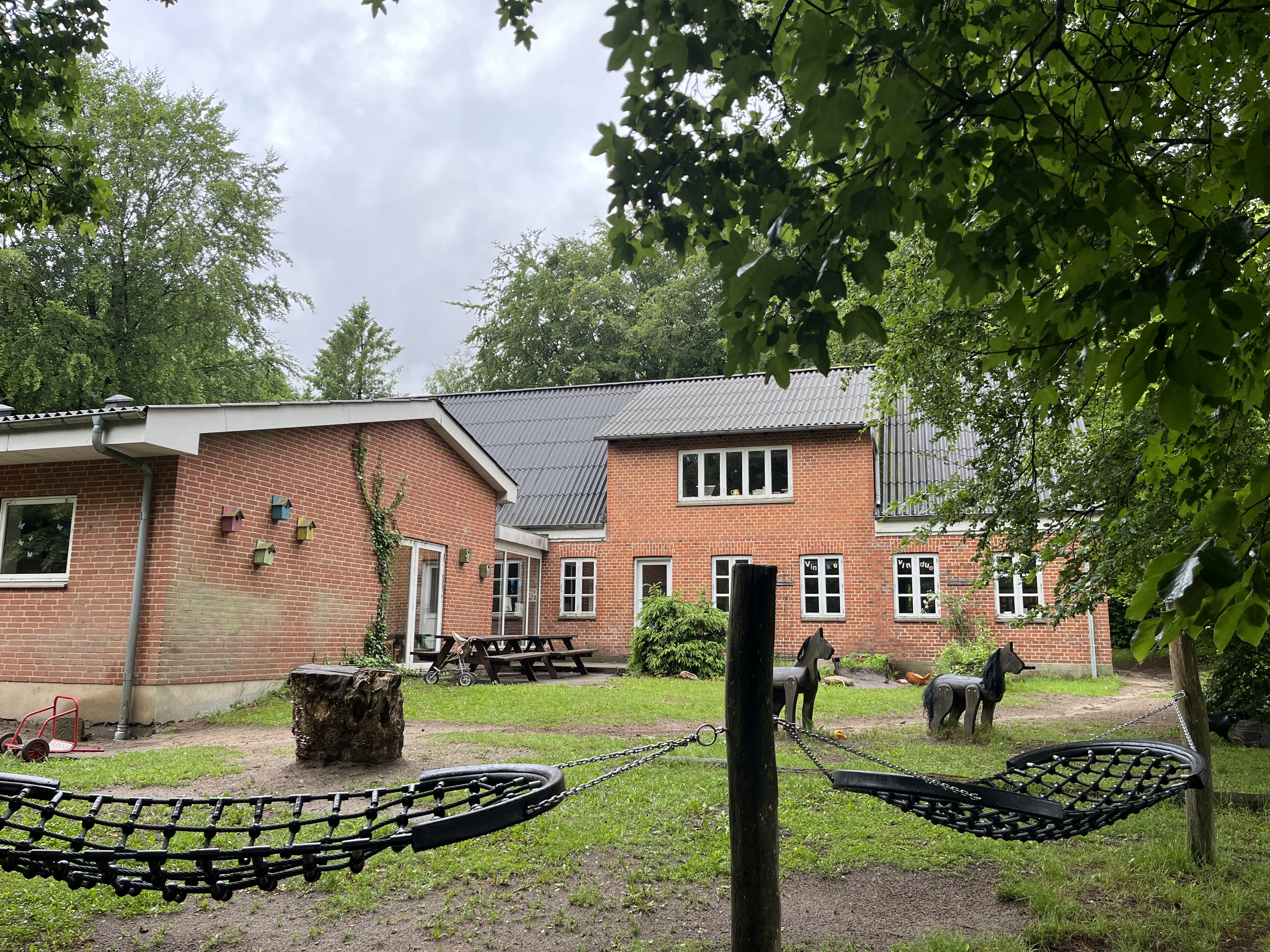 Fredly set ude fra legepladsen, hvor der er masser af grønt skov omkring huset.